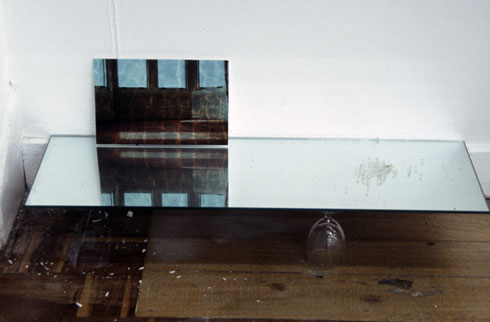 double exposed photograph of a baywindow and water in a swimming pool sitting on a mirrored shelf resting on an upturned wine glass